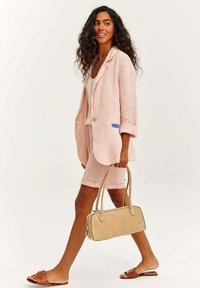 Světle růžový lněný sako s ohrnutými rukávy, odpovídající lněné šortky, hnědé klouzavé sandály a béžová kabelka s dvojitými uchy.