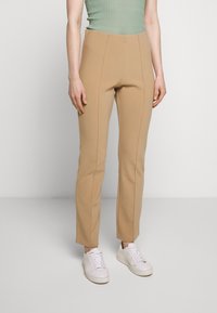 Tan high-waisted pants with a fitted design, featuring vertical seams and a smooth texture, paired with white sneakers.