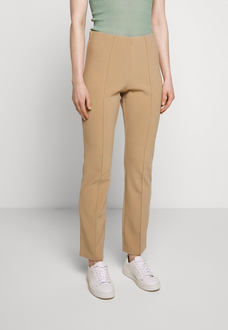 Tan high-waisted pants with a fitted design, featuring vertical seams and a smooth texture, paired with white sneakers.