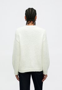 Overdimensjonert hvit genser med strukturert finish, avslappet form, senkede skuldre og ribbestrikkede kanter. Brukes med mørke denimjeans.