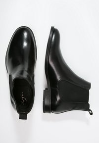 Czarne skórzane buty Chelsea z elastycznymi panelami po bokach, pętelką ułatwiającą zakładanie i płaską podeszwą, o gładkim, polerowanym wykończeniu.