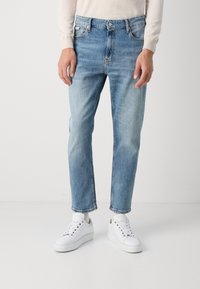 Vaqueros de mezclilla azul claro con corte recto, diseño de cinco bolsillos y costuras visibles. Combinados con zapatillas blancas y un suéter ligero.