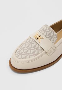 Beige læderloafer med et mønstret tekstilovermateriale og et gyldent MK-logo på remmen. Har en rundet tå og en brun gummisål.