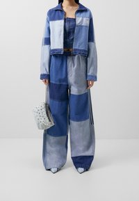 Jeansoutfit med en kort, blockfärgad jacka och matchande vida byxor i olika nyanser av blått; kombinerat med en nitsatt ljusblå väska.