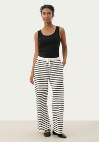 Débardeur noir à encolure dégagée associé à un pantalon ample rayé blanc et noir, avec une taille élastique et un cordon de serrage.