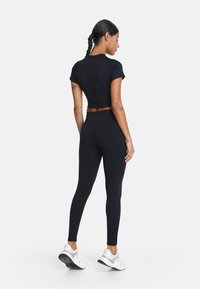 Czarny krótki t-shirt i legginsy wykonane z elastycznego materiału. Posiadają dopasowany fason i bezszwową konstrukcję, w zestawie z białymi butami sportowymi.