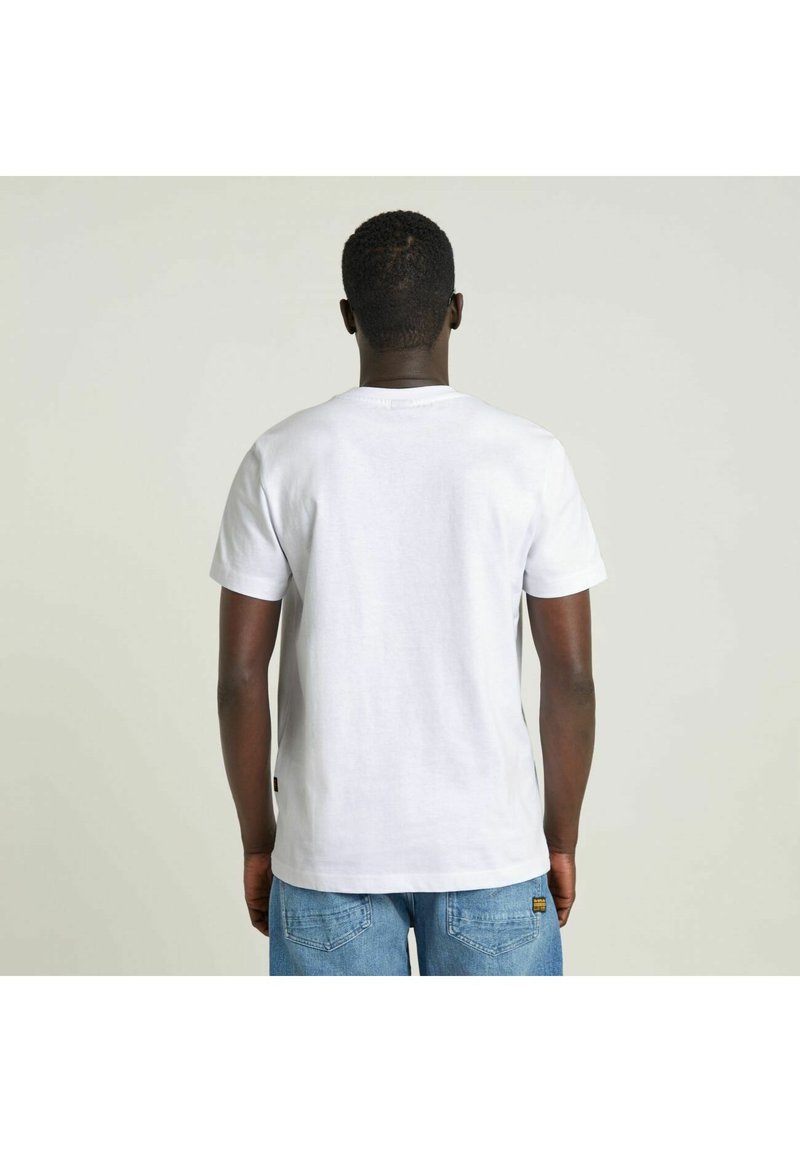 Camiseta blanca de manga corta hecha de algodón, con cuello redondo y dobladillo recto. El modelo lleva puesta unos vaqueros de denim azul.