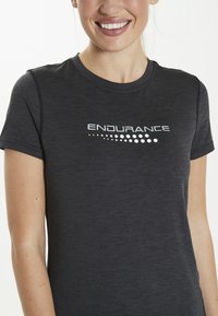 Sort præstations T-shirt med korte ærmer, der har et struktureret stof og et hvidt "ENDURANCE" logo med et prikmønster over brystet.