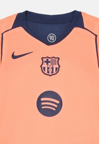 Oranžový športový dres s námorníckym golierom. Obsahuje štítový logotyp, text "FCB" a námornícku Spotify logo na prednej strane. Vyrobený z textúrovanej tkaniny.