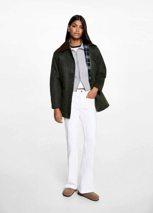 Dark green jacket with suede collar, layered over a grey knit top, paired with white flared jeans and brown slip-on shoes.