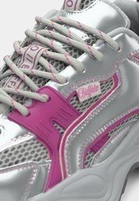 Pantof sport argintiu cu accente roz, cu panouri din plasă, materiale reflectorizante și suprapuneri texturate. Șireturile sunt gri cu detalii roz.
