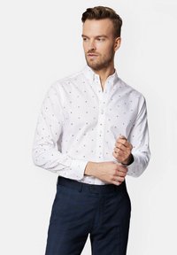 Biała koszula z guzikami, z subtelnym wzorem w kropeczki, z klasycznym kołnierzykiem i długimi rękawami, zestawiona z ciemnymi spodniami w kratę.