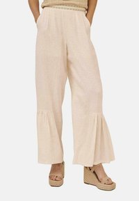 Pantalones de pierna ancha beige claro con una tela texturizada, detalles de plisado en el dobladillo y un corte relajado, combinados con cuñas de plataforma en tono tostado.