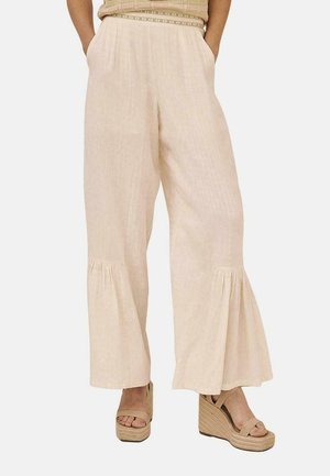 Pantalones de pierna ancha beige claro con una tela texturizada, detalles de plisado en el dobladillo y un corte relajado, combinados con cuñas de plataforma en tono tostado.