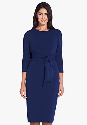 Robe ajustée bleu marine à manches trois-quarts, avec un détail de taille nouée et un ourlet mi-genou. Tissu lisse avec une texture minimale.