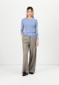 Blauw en wit gestreepte blouse met lange mouwen, gecombineerd met beige wijde broek. De broek heeft een gladde textuur, en de outfit wordt afgemaakt met zwarte schoenen.