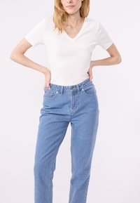 Maglietta bianca a scollo a V abbinata a jeans high-waisted azzurri chiari. La maglietta è aderente, mentre i jeans hanno un design rilassato a gamba dritta.