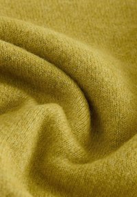Tissu à texture douce avec un tricot fin de couleur jaune moutarde, délicatement plié pour montrer son épaisseur et son motif de tissage.