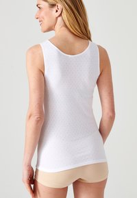 Witte mouwloze tanktop met een textuurpatroon, ronde halslijn en subtiele details. Gecombineerd met beige shorts, weergegeven vanaf de achterkant.