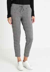 Pantalon à carreaux gris avec une taille à cordon de serrage, coupe ajustée et chevilles retroussées, associé à des baskets blanches et un haut noir à manches longues.