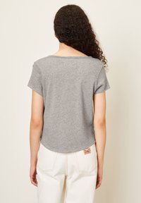 Pilkas trumpas marškinėliai, pagaminti iš minkštos medvilnės, su trumpomis rankovėmis, turi apvalų iškirpimą ir žalią kraštą, derinami su baltais kelnais.