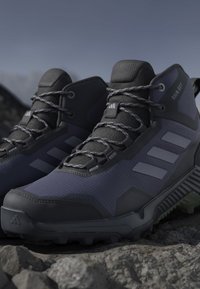 Dark gray and black high-top hiking shoes with textured soles and laces, placed on rocky ground outdoors.