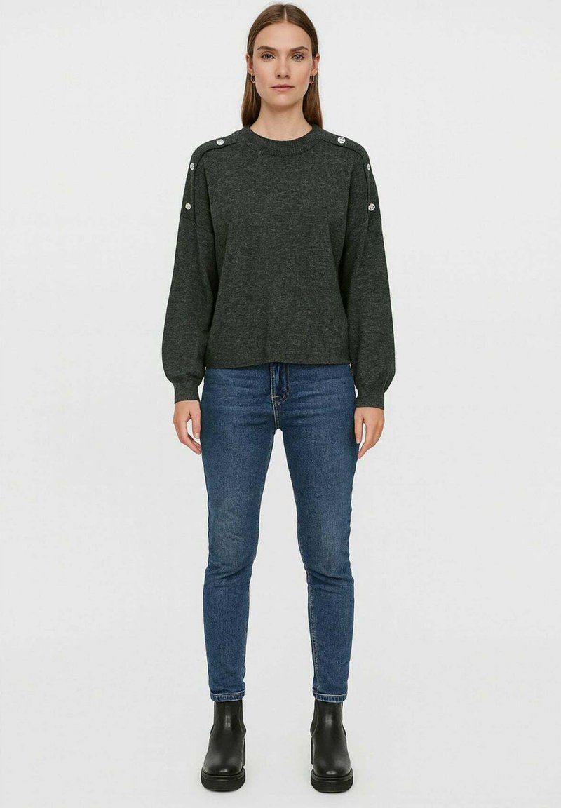Maglione pullover grigio scuro con collo rotondo, maniche lunghe e dettagli con bottoni sulle spalle, abbinato a jeans skinny blu e stivaletti neri.