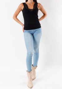 Top sin mangas negro con borde de encaje, combinado con pantalones ajustados de mezclilla azul claros y botas cowboy beige, mostrando una silueta ajustada y acentos texturizados.