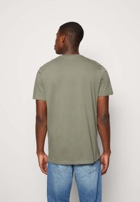 Tricou scurt cu mânecă scurtă de culoare verde măslinie, fabricat din bumbac, cu guler rotund și o croială lejeră, asociat cu blugi decolorati de culoare albastră deschisă.
