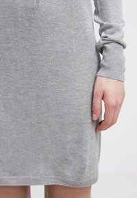 Abito lavorato a maglia grigio chiaro con maniche lunghe, caratterizzato da una texture a coste, corpino aderente e leggero arricciamento ai polsi.