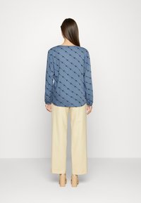 Camisa azul de manga longa com um padrão negro repetitivo, emparelhada com calças largas creme e sapatos nude de salto grosso.