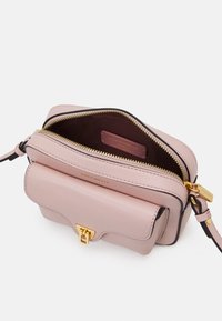 Kompaktowa różowa skórzana torebka z złotymi akcentami, zamykana na zamek błyskawiczny, z przednią kieszenią na klapkę. Wnętrze wykończone ciemnym materiałem z detalem marki.