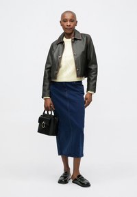 Veste en cuir noire cropped, pull en tricot crème, jupe midi en denim bleu, sac à main noir avec détail circulaire, chaussures noires à enfiler.