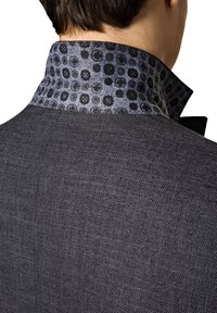 Czarna blazerka o teksturowanej powierzchni z wzorzystym szarym kołnierzem. Kołnierz zdobi czarny kwiatowy wzór na szarym tle.