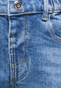 Tissu en denim bleu avec un effet délavé, doté d'une poche avant, de coutures orange et d'un bouton métallique à la taille.