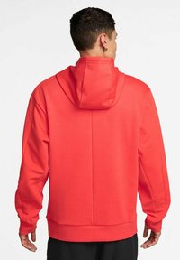 Felpa rossa con cappuccio regolabile, vestibilità comoda, texture morbida e polsini e bordo a costine. Senza loghi o fantasie visibili.