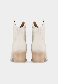 Ζευγάρι μπεζ μποτάκια αστραγάλου με υφή στην επάνω επιφάνεια και τακούνια από στοιβαγμένο ξύλο, από πίσω σε ένα απλό λευκό φόντο.