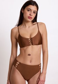 Completo bikini marrone con design a lacci al centro del top e dettagli laterali sui pantaloni a vita alta. Tessuto liscio e testurizzato.