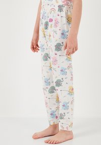 Valkoiset pyjamahousut, joissa on värikkäitä sarjakuvahahmoja ja kuvioita, kuten norsuja, sateenkaaria, kukkia ja leikkisiä yksityiskohtia. Joustava vyötärönauha.