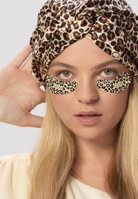 Opaski na oczy w panterkę na modelce z długimi, prostymi blond włosami, noszącą turban w panterkę i jasną bluzkę.