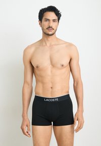 Black cotton boxer briefs with a contrasting white "LACOSTE" logo on the waistband. The design features a fitted shape and soft texture.