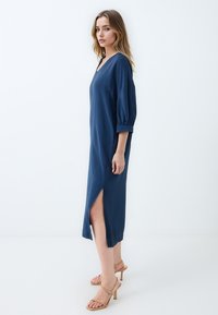 Abito blu navy, lungo fino al ginocchio, con scollatura a V, maniche corte a palloncino e spacco laterale. Realizzato in tessuto leggero, presenta una vestibilità ampia.