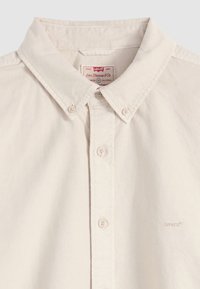 Chemise beige à boutons avec col boutonné, quatre boutons visibles et petit logo Levi's brodé sur la poitrine.