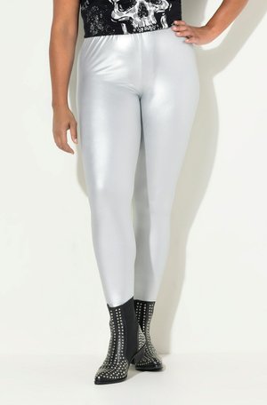 Zilveren, glanzende leggings met een gladde textuur, gecombineerd met zwarte, gespijkerde enkellaarsjes met een taps toelopende vorm en een lage hak.
