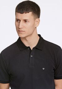 Polo nero realizzato in tessuto testurizzato, con colletto classico, patta con due bottoni e un piccolo logo bianco sul petto.