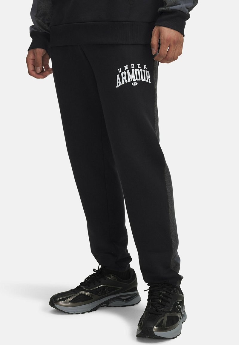 Black sweatpants with a tapered fit, featuring a white "UNDER ARMOUR" logo. Made from soft fabric with a side stripe detail.