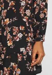 Luźna czarna sukienka z kwiatowym nadrukiem w ciepłych odcieniach. Posiada długie rękawy, warstwowy dół i miękką tkaninę. Szczegóły obejmują falbany i elastyczne manszety.
