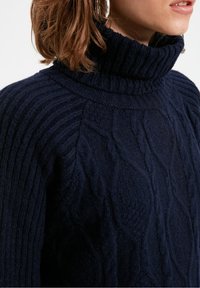 Námořnická modrá pletená svetr s vysok�ým žebrovaným rolákem. Obsahuje texturované vzory a volný střih. Vyrobeno z měkkého a útulného materiálu.