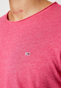Pink cotton t-shirt with a round neckline and short sleeves. Features a small embroidered logo on the chest and a textured, mottled finish.