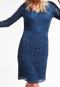 Robe en dentelle marine à manches longues, dotée de motifs floraux et d'un décolleté en V, se terminant au-dessus du genou avec un ourlet en forme de vagues.